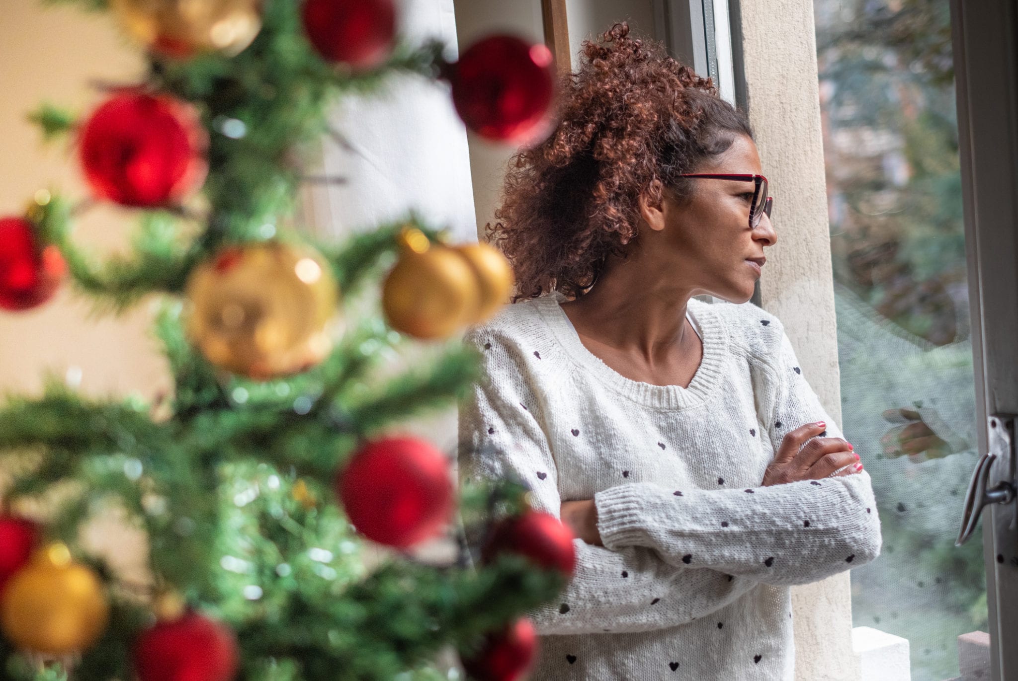 A woman looks out a window pensively during Christmas.